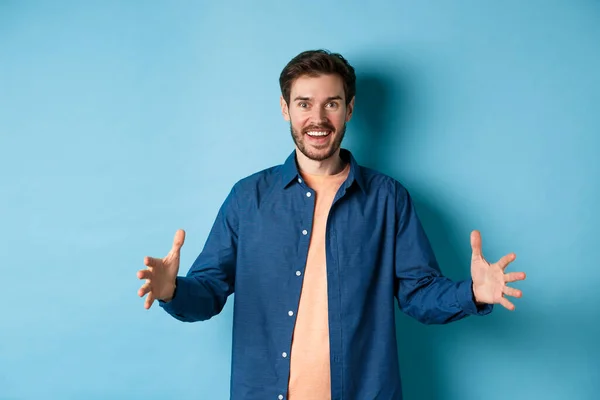 Gelukkig glimlachende man tonen grote grootte object, vormgeven van grote ding en kijken verbaasd, staan op blauwe achtergrond — Stockfoto