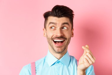 Sevgililer Günü konsepti. Romantik bir adam kalbini gösteriyor ve sola bakıyor, gülümsüyor mutlu, pembe arka planda duruyor rüya gibi.