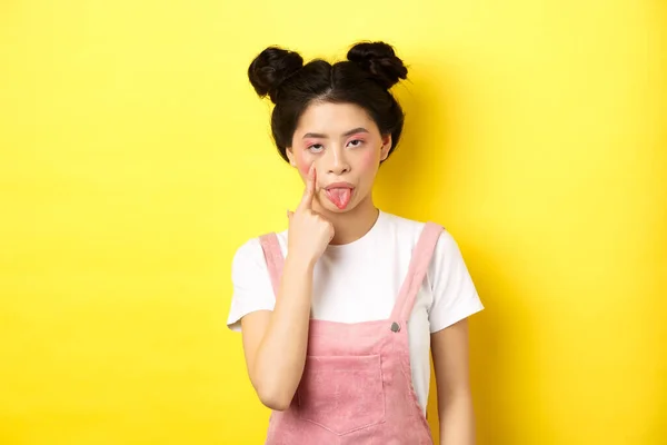 Rude κορίτσι της Ασίας τεντώσει βλέφαρο και δείχνει γλώσσα, κοροϊδεύοντας κάποιον, στέκεται σε κίτρινο φόντο — Φωτογραφία Αρχείου