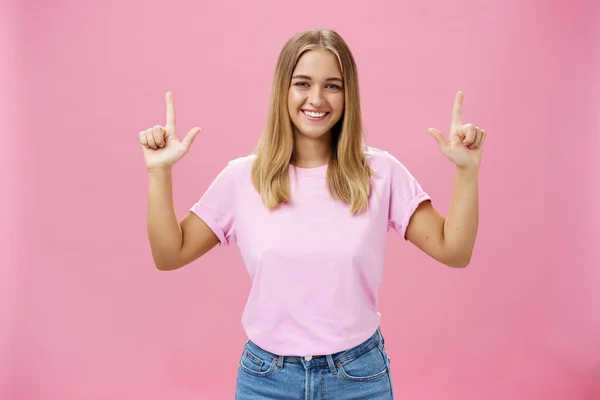 Wewnętrzne ujęcie atrakcyjnej, przyjaznej dziewczynie z opaloną skórą w luźnym t-shircie i dżinsach podnoszących ręce do góry i uśmiechających się szeroko do kamery z satysfakcjonującym spojrzeniem na różowe tło — Zdjęcie stockowe