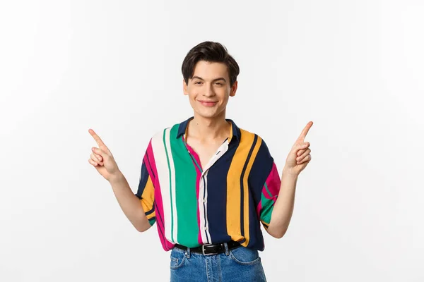 Handsome queer man pointing fingers sideways, smiling pleased and showing two choices, standing over white background — Stock Photo, Image