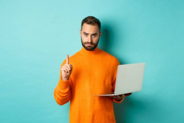 Yetişkin bir adamın online öğretmenlik yaparken, dizüstü bilgisayar kullanırken parmağını göstermesi, kuralları açıklaması, açık mavi arka planda durması