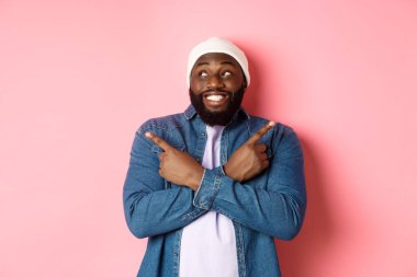 Heyecanlı genç Afro-Amerikalı adam iki seçenek gösteriyor ve karar veriyor, mutlu bir şekilde gülümsüyor, pembe arka planda duruyor.