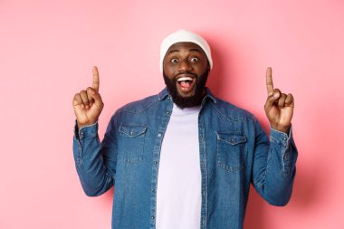 Neşeli siyahi adam harika bir reklam sunuyor, parmaklarını havaya kaldırıyor ve gülümsüyor, pembe arka planda duruyor.