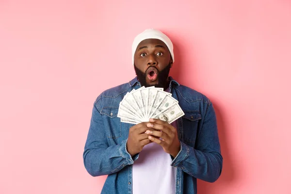 Incroyable homme afro-américain recevoir un prix en espèces, montrant de l'argent et regardant la caméra dans la crainte, debout sur fond rose — Photo