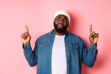 Üzgün ve kasvetli, bereli Afro-Amerikan adam, parmaklarını havaya kaldırıyor, iç çekiyor ve üzüntü ile en üste bakıyor, pembe arka planda duruyor.