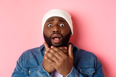 Şok olmuş ve korkmuş Afrikalı-Amerikalı adam kameraya bakıyor, endişeli, pembe arka planda duruyor.