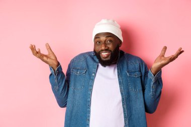 Siyahi bir adam omuz silkiyor ve kameraya bakıyor. Bilmiyorum, pembe arka planda kararsız duruyor.