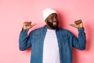 Hipster bereli ve kot gömlekli, kendine güvenen yüzüyle pembe arka planda duran kendine güvenen siyah sakallı adam.