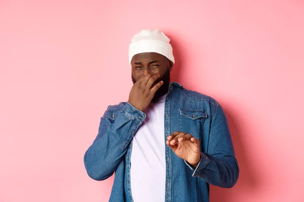 Ekelhafter schwarzer Mann hält Nase zu und weint vor furchtbarem Geruch, zeigt Verweigerungsgeste, steht über rosa Hintergrund — Stockfoto