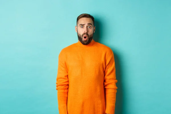 Shocked and confused man looking in awe at promo offer, standing near copy space on turquoise background — Stock Photo, Image