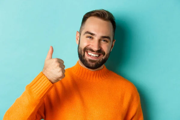 Close-up of attractive young man showing thumb-up, praising good work, standing over light blue background, giving positive answer — Stock Photo, Image