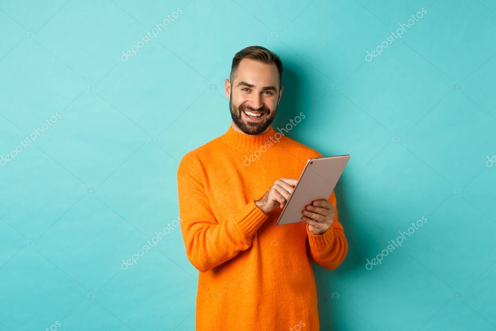 Handsome adult man using digital tablet and smiling, shopping online, standing over light blue background.