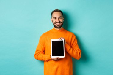 Teknoloji. Gülümseyen yakışıklı adam dijital tablet ekranı gösteriyor, uygulamayı gösteriyor, turkuaz arka planda duruyor