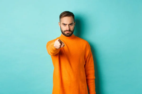Confident man blame you, frowning and pointing finger at camera, accuse person, judgemental stare, standing over light blue background — Stock Photo, Image