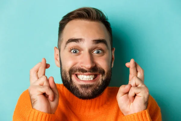 Headshot de homem barbudo esperançoso fazendo um desejo, sorrindo e segurando os dedos cruzados para boa sorte, de pé sobre fundo azul claro — Fotografia de Stock