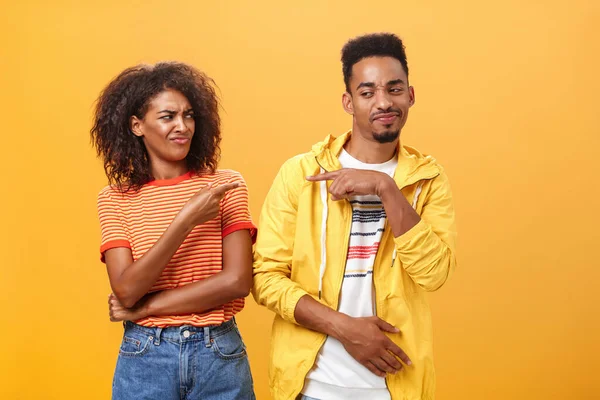 Two best friends fooling around having fun pointing at each other with cute joyful smile as if blaming each other playfully. Cute female looking at boyfriend standing together over orange wall — Stock Photo, Image