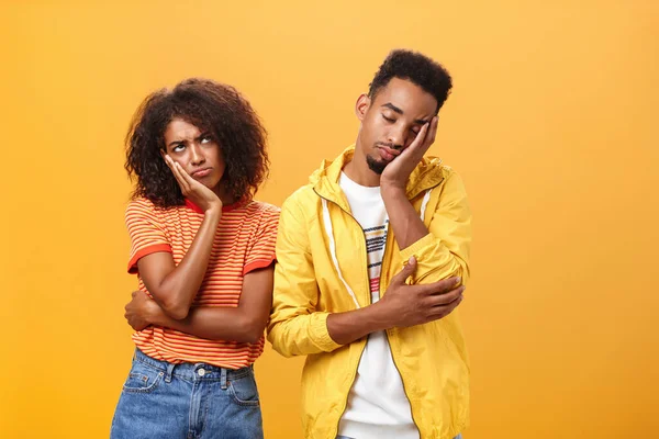 Girl feeling displeased and offended on boyfriend who fell asleep during date pursing lips frowning looking up while boyfriend leaning head on face with closed eyes and tired look over orange wall — Stock Photo, Image