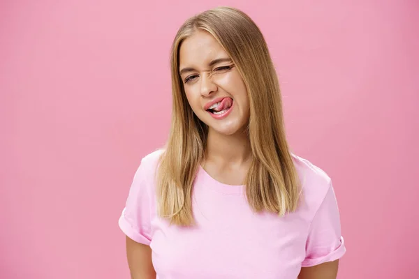 Speels flirterig aantrekkelijk jong meisje met mooi recht haar in t-shirt knipperen op camera glimlachen en likken bovenlip met tong gevoel enthousiast en zorgeloos tegen roze achtergrond — Stockfoto