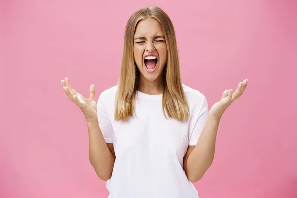 Woman feeling fed up having mental breakdown during deadline yelling with closed eyes, raising hands aside in pissed gesture feeling distressed and pressured losing temper over pink wall — Stockfoto