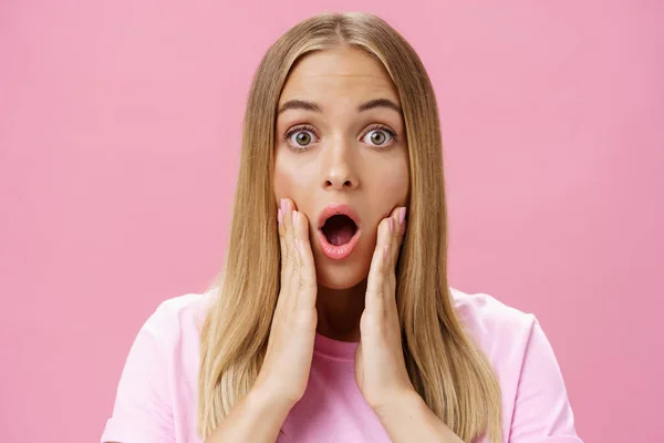 Крупним планом знімок шокованої молодої студентки-жінки з засмаглою шкірою і справедливим волоссям, що падає щелепа, що дме з подиву, торкаючись щоки, здивовані реакцією на шокуючі приголомшливі новини на рожевому фоні — стокове фото