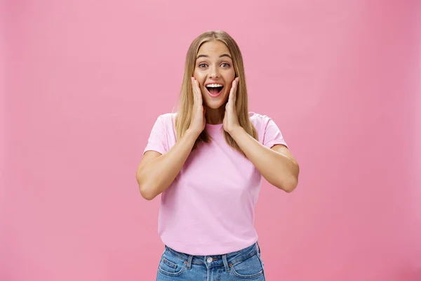Задоволена і здивована щаслива дівчина в футболці і джинсах, посміхаючись широко з відкритим ротом розважаються зворушливі щоки здивовані і задоволені реагують на позитивний сюрприз на рожевому фоні — стокове фото