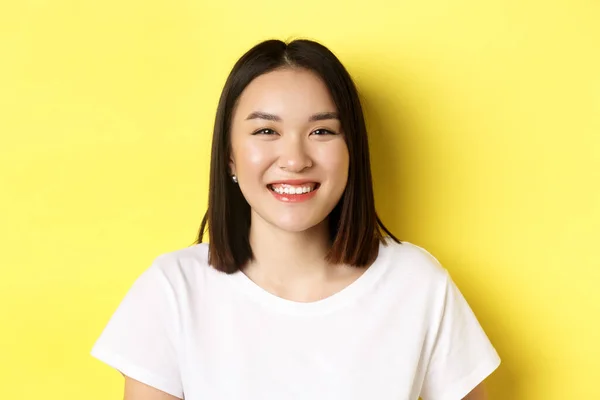 아름다움. 웃고 있는 귀엽고 귀여운 동양 여성이 완벽 한 흰색 미소 이빨과 밝은 피부를 갖고 티셔츠를 입고 노란 배경 위에 서 있는 모습 — 스톡 사진