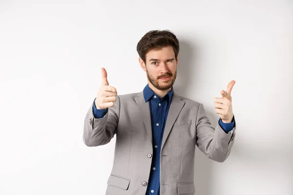 You got this. Handsome caucasian businessman in suit pointing fingers at camera and winking, motivating people, inviting to work in company, standing on white background — Stock Photo, Image