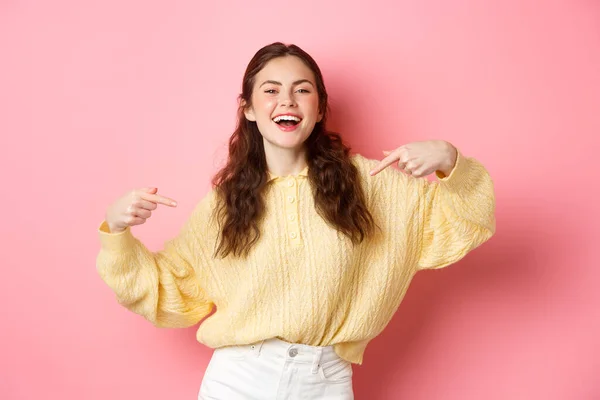 Chica feliz seguro de sí mismo señala a sí misma y se ríe, auto-promoción y sonriendo, de pie sobre fondo rosa —  Fotos de Stock