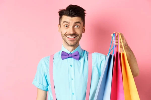 Imagen de tipo feliz en las compras, sosteniendo bolsas de papel y sonriendo emocionado, comprador compra con descuentos, de pie sobre fondo rosa —  Fotos de Stock