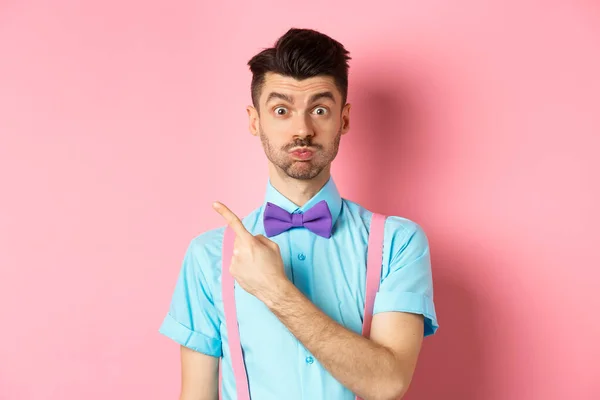 Вражений молодий чоловік демонструє чудову промо-пропозицію, піднімає брови і виглядає зацікавленим, вказуючи пальці у верхньому лівому куті, рожевий фон — стокове фото