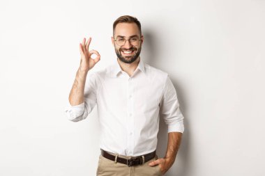 Tatmin olmuş iş adamı gülümsüyor ve işaret veriyor, onaylıyor ve beyaz arka planda duran iyi bir şey gibi.