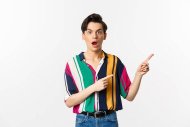 Etkilenmiş genç bir adam reklamını yapıyor, ağzı kulaklarıyla açık ve sağ üst köşeyi işaret ediyor, beyaz arka planda duruyor.