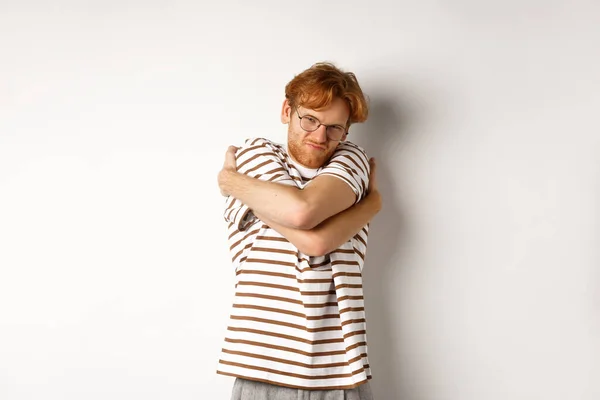 Reluctant young man with messy red hair unwilling do something, hugging himself and grimacing, standing over white background — Stock Photo, Image