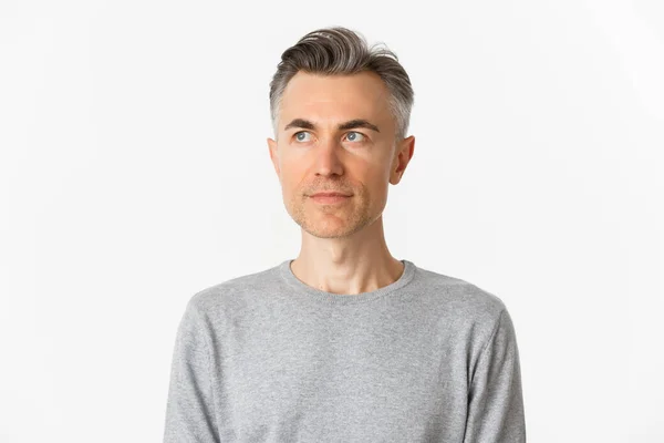 Close-up van knappe man van middelbare leeftijd in grijze trui, kijkend naar linksboven, staande over witte achtergrond — Stockfoto