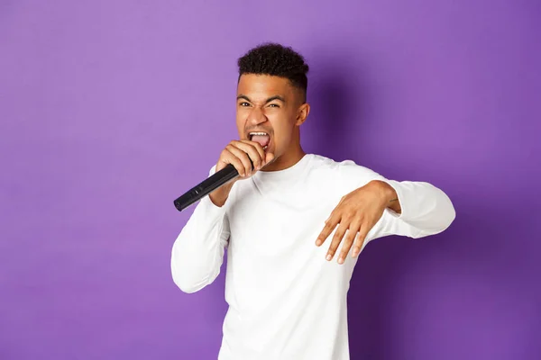 Obrázek drzého afroameričana zpívajícího v mikrofonu, jak rapuje a vystupuje na jevišti, stojí nad fialovým pozadím — Stock fotografie
