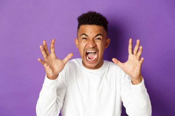 Image of pissed-off african american guy yelling at someone, raising hands and looking with hatred and anger, standing over purple background — Stockfoto