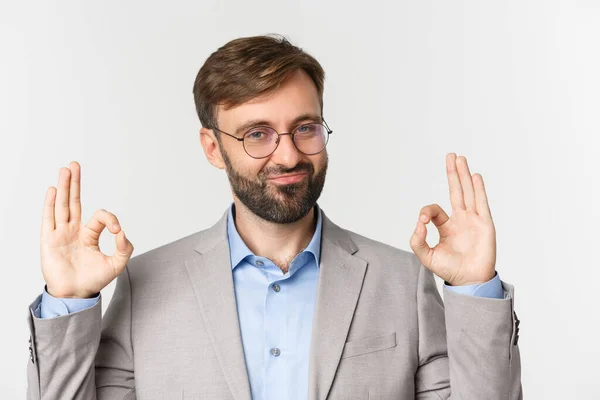 Primer plano del jefe impresionado en traje gris y gafas, mostrando signo de bien y sonriendo, dar aprobación, alabanza buen trabajo, de pie sobre fondo blanco — Foto de Stock