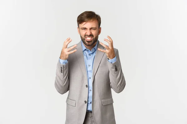 Porträt eines bärtigen männlichen Angestellten im grauen Anzug, der sich beschwert und Hände schüttelt, wütend guckt, Arbeit hasst, vor weißem Hintergrund steht — Stockfoto