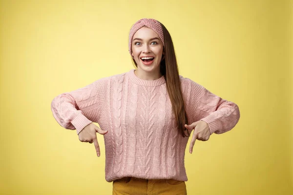 Euphoric ελκυστική νεαρή μοντέρνα κοπέλα στην πλεκτή μπάντα φορώντας πουλόβερ χαμογελώντας ενθουσιασμένοι δείχνοντας κάτω ενθουσιασμένοι από την τρομερή προώθηση στέκεται διασκεδάζει και συγκλονισμένοι πάνω από κίτρινο φόντο — Φωτογραφία Αρχείου