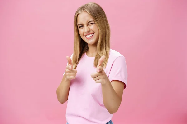 Donna che esprime un atteggiamento positivo verso la fotocamera puntando con le dita e strizzando l'occhio gioiosamente sorridente essere sollevato, in piedi di buon umore con gesti ottimisti sullo sfondo rosa — Foto Stock