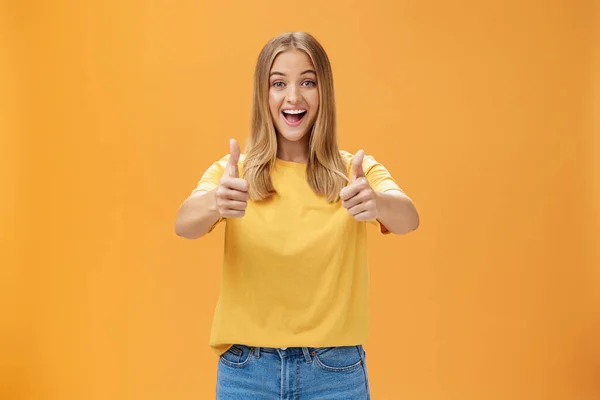 女人竖起大拇指，开心地微笑着，表现出积极向上的态度，就像在概念或想法上表示赞同，在橙色的背景下显得快乐而快乐 — 图库照片