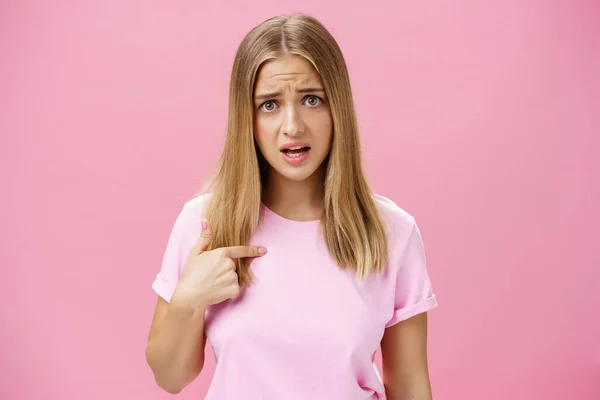 Insulted girl pointing at herself with displeased pissed and questioned expression asking question being shocked she picked or accused in something terrible and disrespectful posing against pink wall —  Fotos de Stock