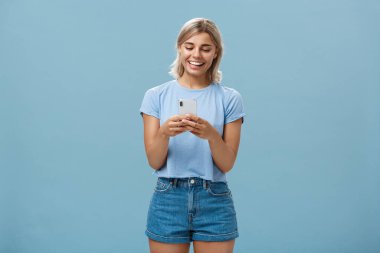 İnternet arkadaşlarının olması güzel. Dertsiz, mutlu, sarışın, bronz tenli, sarışın, akıllı telefondan mesaj okuyan, mavi duvardan memnun bir bayan öğrenci.