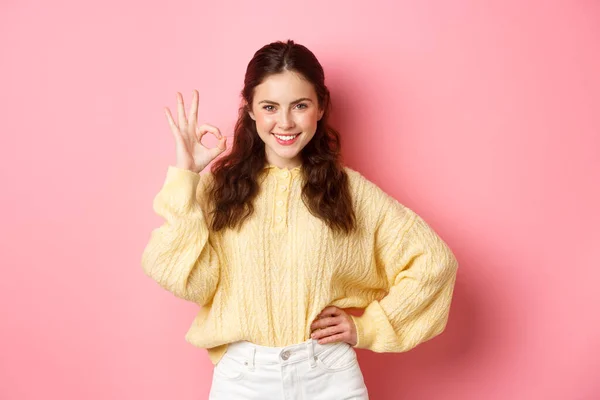 Retrato de jovem mulher confiante sorrindo satisfeito, dizer sim ao mostrar sinal ok, dar aprovação, louvor excelente escolha, de pé contra fundo rosa — Fotografia de Stock