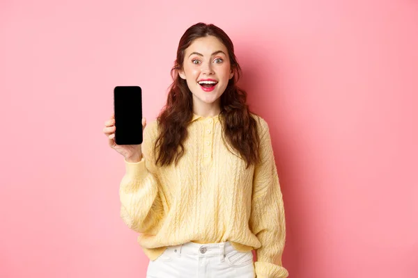 Teknik och näthandel. Attraktiv kvinna student ser upphetsad, visar tom smartphone skärm och leenden, står mot rosa bakgrund — Stockfoto