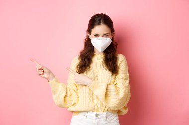 Covid, Corona ve sosyalleşme konsepti. Gülümseyen, düşünceli, parmaklarını logo afişini gösteren, karantina sırasında tıbbi solunum cihazı takan, pembe arka plan...