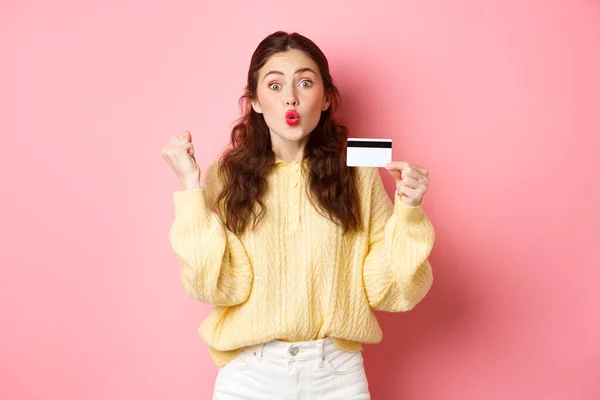 Возбужденная девушка-покупатель говорит да, делает кулачный насос и выглядеть изумленным, показывая пластиковые кредитные карты и готовы к покупкам, стоя на розовом фоне — стоковое фото