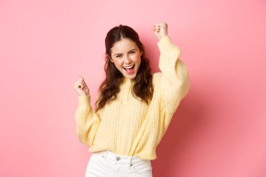 Neşeli mutlu kadın hedefe ulaşır, başarıyı kutlar, evet der ve dans eder, zafer dansı yapar, pembe arka planda durur.