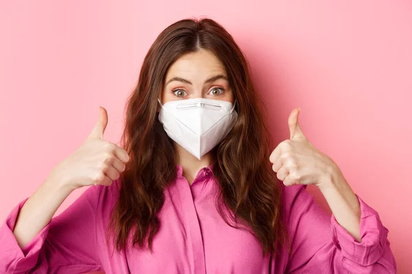 コロナウイルス,予防措置と健康の概念.幸せな美しい女性で医療用マスクからcovid-19,ショー親指アップで承認,賞賛良い選択,ピンクの背景 — ストック写真